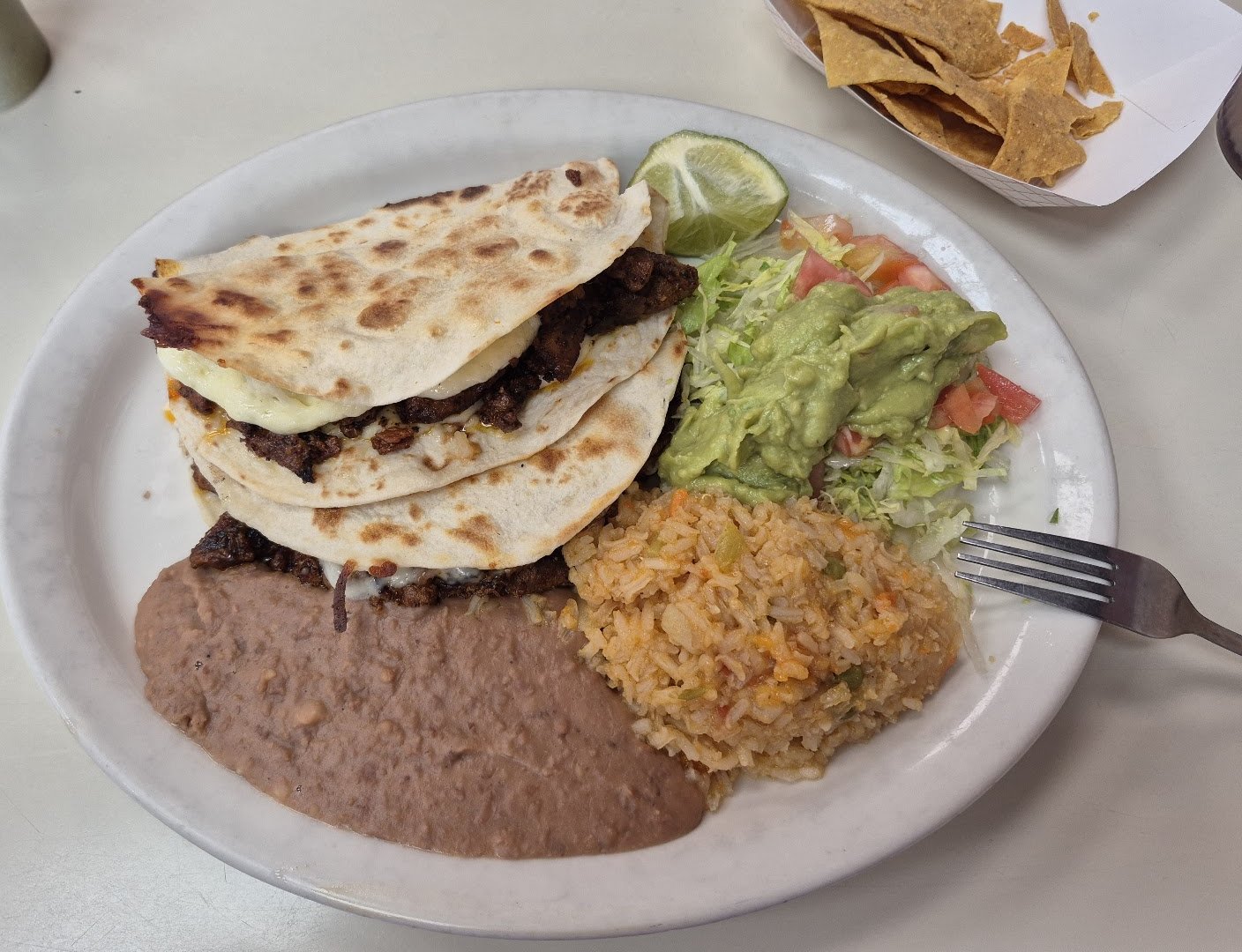 Plate of three asada quesadillas on grilled flour tortillas with melted cheese and carne asada, with refried beans, Mexican rice, guacamole, lettuce and tomato