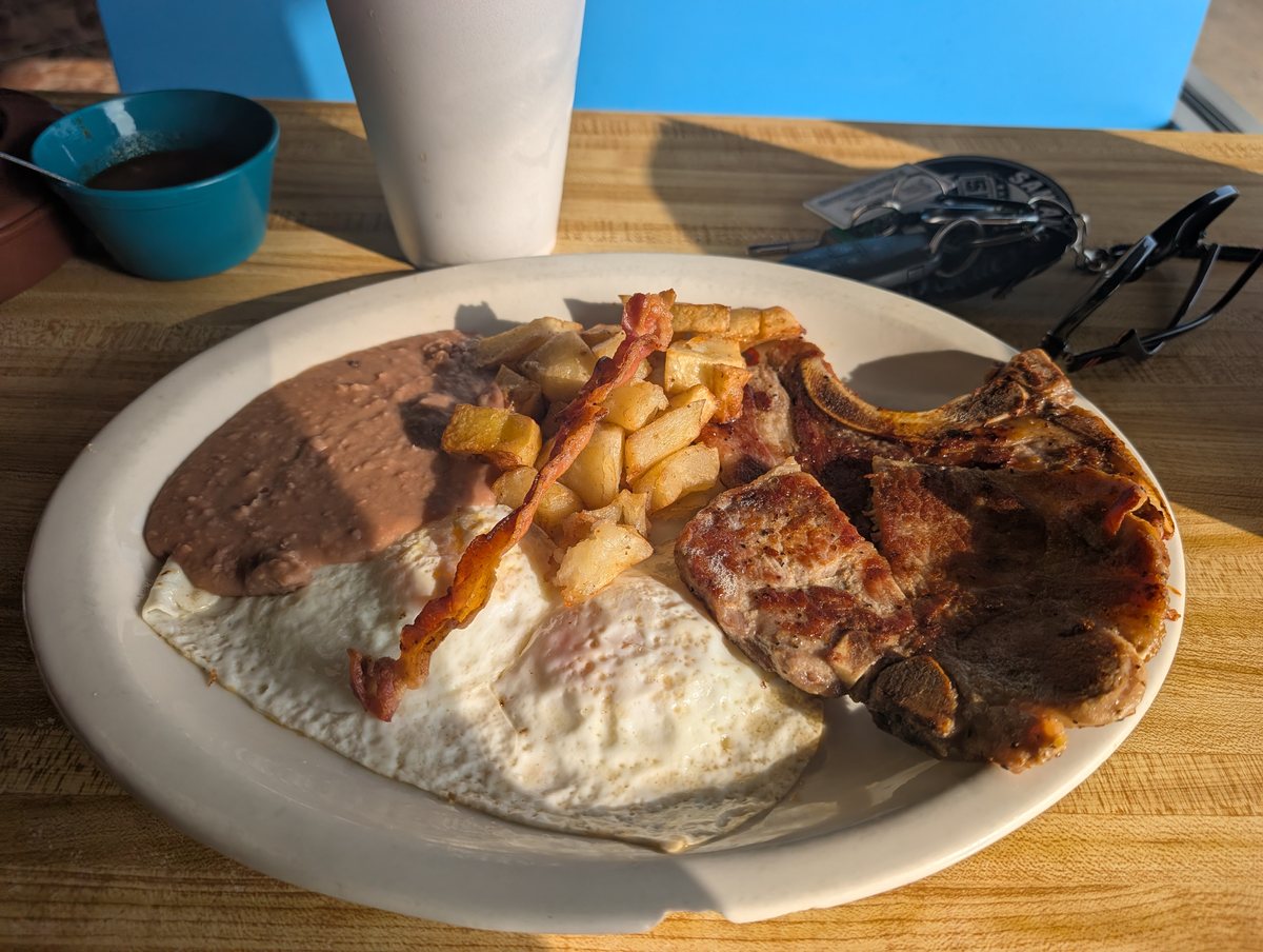 Pork chop and eggs: a bone-in pork chop with fried eggs, bacon, fried potatoes and refried beans