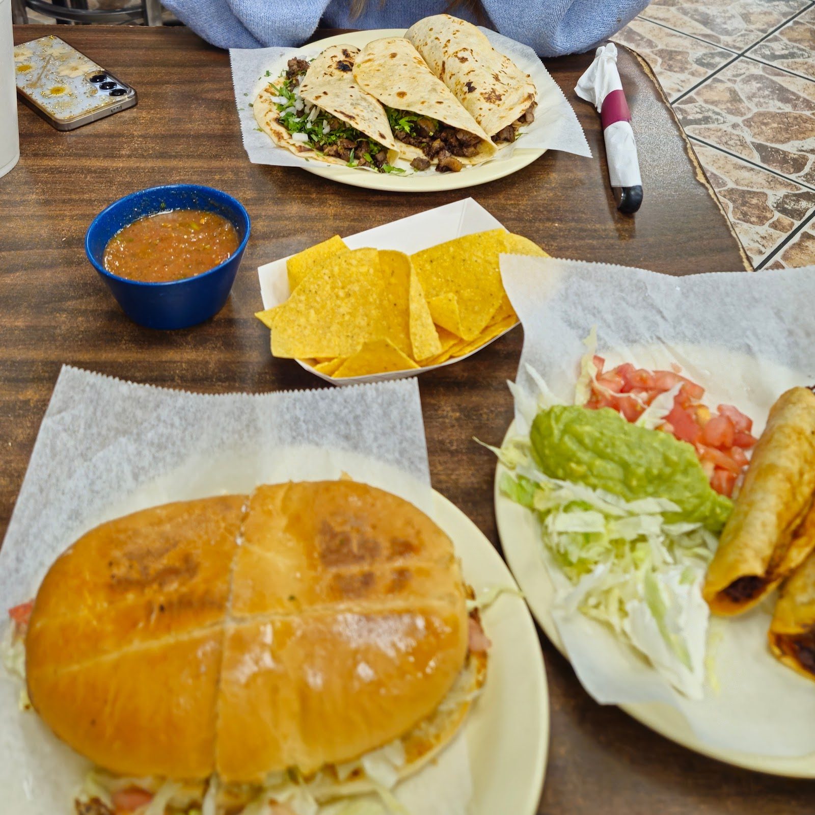 Torta, tacos, flautas with guacamole, chips and salsa on a table
